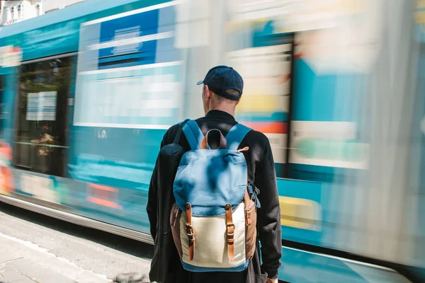 Mann steht vor Straßenbahn. Männliche Touristen in Freizeitkleidung mit Rucksack stehen an einem sonnigen Sommertag vor der Straßenbahn. Bewegungsunschärfe. — Stockfoto