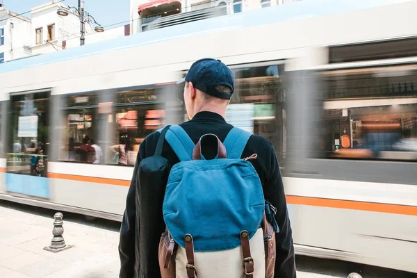 Yol tramvay ile önünde dostum. Sırt çantası ile rahat kıyafetler erkek turist önünde duruyor yol tramvay ile güneşli yaz günü geçiyor. Hareket Bulanıklığı.
