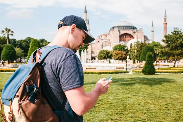 Путешественник с рюкзаком на площади Султанахмет возле знаменитой мечети Айя София в Стамбуле в Турции. Он посмотрит на телефонную карту города и позвонит. Туризм, достопримечательности — стоковое фото