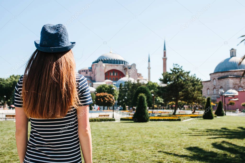A young girl traveler in a hat from the back in Sultanahmet Square next to the famous Aya Sofia mosque in Istanbul, Turkey. Travel, tourism, sightseeing.