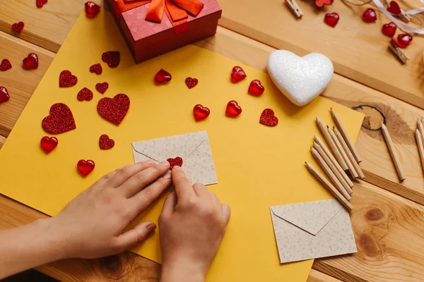 The girl wrote a letter with congratulations and pastes the envelope with a symbol in the form of a heart. Nearby lie various objects symbolizing the event. — Stock Photo, Image