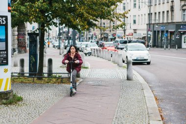 Berlin, 12 Aralık 2017: Bir kız bir scooter üzerinde bir özel bisiklet yol boyunca şehrin bina, yol, araba yanındaki sokak sürmek. Şehrin her yerinde ulaşım araçlarının çevre dostu.