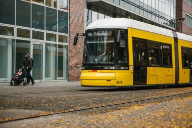 Berlin, 12 Aralık 2017: şehrin sokak hareket bir geleneksel modern sarı tramvay. Bir baba küçük bir çocukla yürüyor. Avrupa'daki sıradan şehir yaşamı.