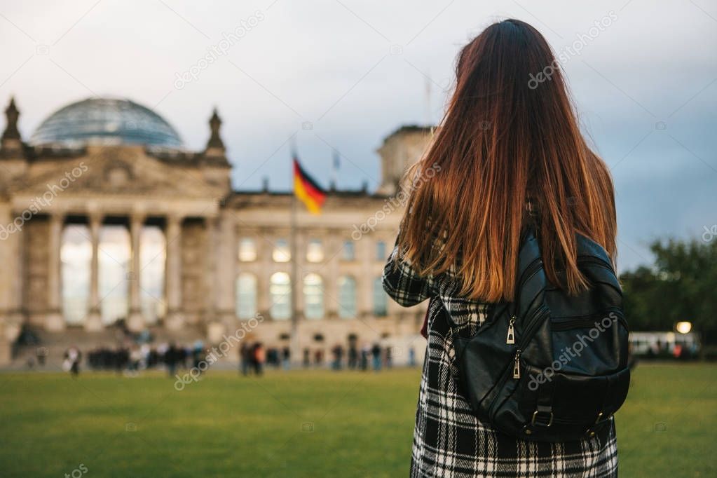 A tourist girl with a backpack next to the building called the Reichstag in Berlin in Germany takes pictures. Sightseeing, tourism.