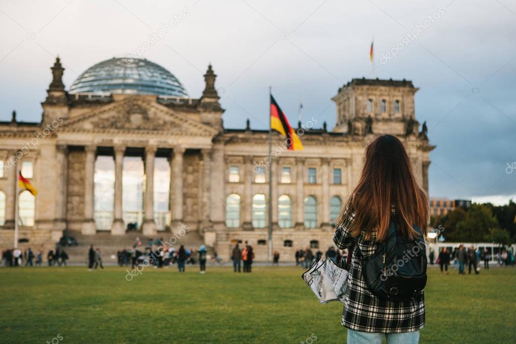 A tourist girl with a backpack next to the building called the Reichstag in Berlin in Germany takes pictures. Sightseeing, tourism, travel around Europe
