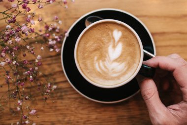 A mans el tutar bir fincan kahve ile bir ahşap yüzeye yakın çiçekler.