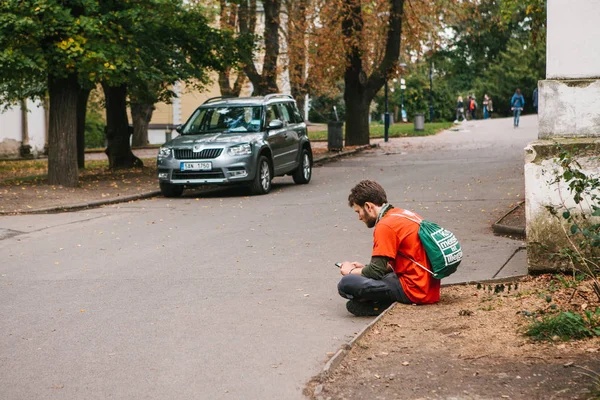 Praga, 25 settembre 2017: Un giovane turista con uno zaino è seduto per strada e comunica con uno smartphone con gli amici . — Foto Stock