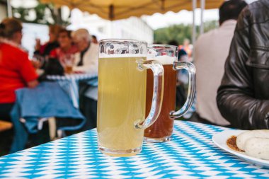 Açık ve koyu bir bira ile iki bardağı masaya dur. Arka planda insanlar bulanık. Geleneksel Alman Bira Festivali kutlama Oktoberfest denilen