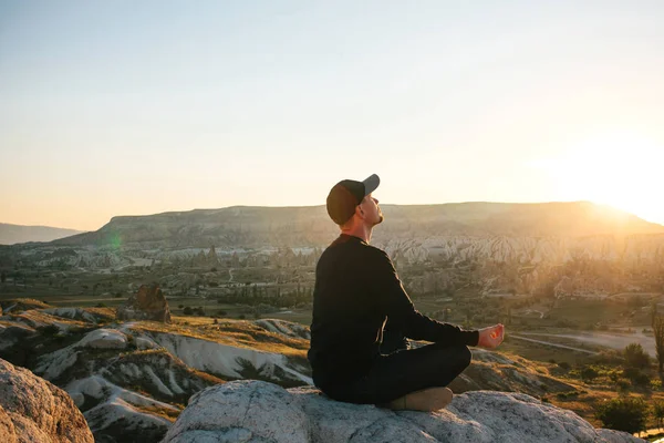 Bir adam güneş doğarken dağın zirvesine yoga uygulamaları. Gevşeme uygulamaları.