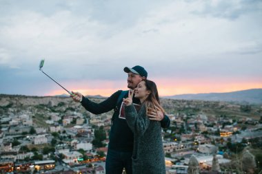 Güzel bir çift şehir Göreme Kapadokya Türkiye'de fon karşı gün batımında selfie yapıyor.