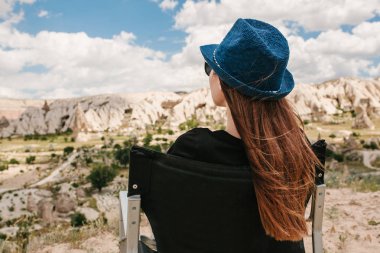 Kız bir sandalyede oturur, rahatlatır ve Türkiye'de Kapadokya'nın eteklerindeki muhteşem bir görünüm hayran. Gevşeme, dinlenme, tatil, seyahat.
