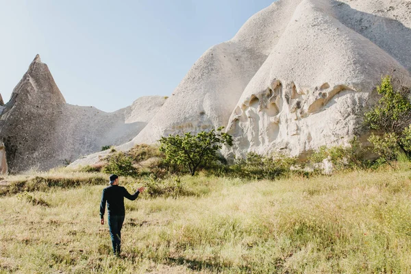 El hombre se encuentra junto a las hermosas rocas y admira el paisaje en Capadocia en Turquía y señala una de las colinas. El paisaje de Capadocia . —  Fotos de Stock