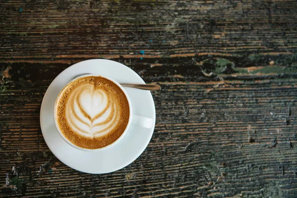 Vista dall'alto. Una tazza di delizioso caffè cappuccino profumato con schiuma e impastatrice su una superficie di legno . — Foto Stock
