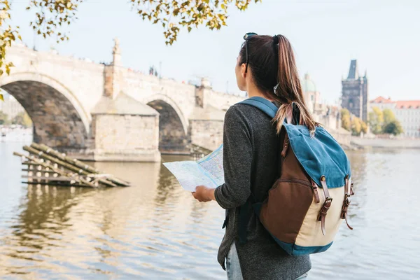 Krásná mladá dívka stojí a dívá na mapě vedle řeky Vltavy s úžasnou starou architekturou Prahy v pozadí a slunný jarní den — Stock fotografie