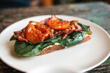 Jambon, kızarmış domates ve yeşillik ahşap bir masa üzerinde bir tabakta lezzetli ve besleyici sandviç.