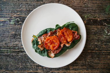 Üstten Görünüm. Jambon, kızarmış domates ve yeşillik bir ahşap yüzeyde bir tabakta lezzetli ve besleyici sandviç.