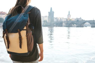 Bir sırt çantası bir güzel genç turist kızla Prag'da Vltava Nehri yanındaki duruyor ve Charles Köprüsü denilen en popüler konumlar hayran. Çek Cumhuriyeti seyahat.
