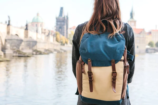 Krásné mladé turistické dívka s batohem stojí u řeky Vltavy v Praze a jednou z nejoblíbenějších atrakcí nazývá Karlův most obdivuje. Cestování po České republice. — Stock fotografie