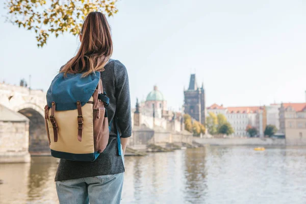 Bir sırt çantası bir güzel genç turist kızla Prag'da Vltava Nehri yanındaki duruyor ve Charles Köprüsü denilen en popüler konumlar hayran. Çek Cumhuriyeti seyahat.