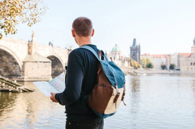 Bir sırt çantası ayakta Prag'da Vltava Nehri yanındaki genç turist adamla Haritaya benziyor ve şehir'in mimaride hayran. Charles Köprüsü yakındır. Çek Cumhuriyeti seyahat.