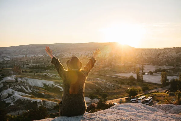 Een toeristische meisje in een hoed zit op een berg en kijkt naar de zonsopgang. — Stockfoto