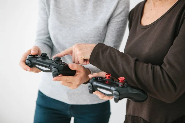 The elderly woman asks the young girl how to use the joystick for video games and shows her finger on the buttons. Modern technologies and people. Teaching older generation the use of technology.