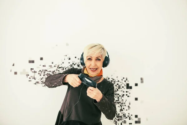 An elderly woman plays a video game and is fragmented into pixels. A conceptual photo with visual effects meaning an elderly person and new technologies.