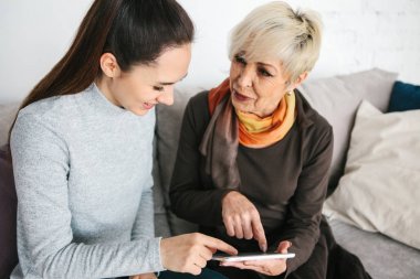 Bir genç kız yaşlı bir kadın için bir tablet kullanımını açıklar veya bir uygulama gösterir veya bir sosyal ağ kullanmayı öğretir. Yeni teknolojilerin eski nesil öğretim.