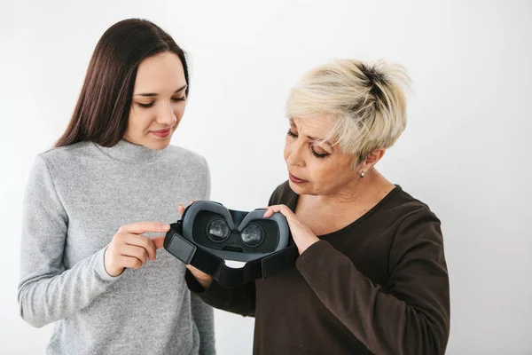 Una joven le explica a una anciana cómo usar gafas de realidad virtual. La generación más antigua y las nuevas tecnologías . — Foto de Stock