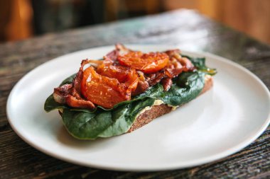 Jambon, kızarmış domates ve yeşillik ahşap bir masa üzerinde bir tabakta lezzetli ve besleyici sandviç.