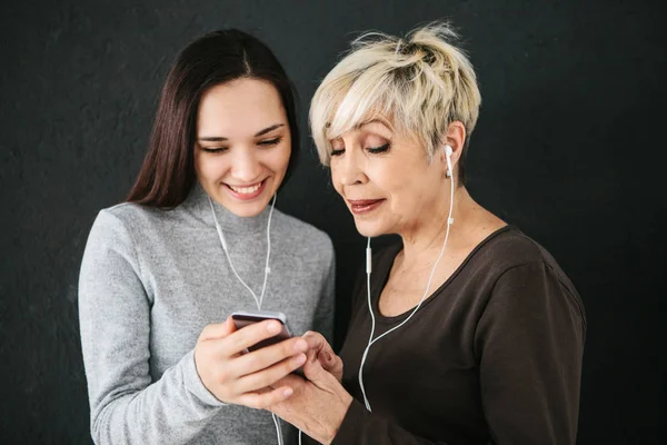 Uma mulher idosa e uma jovem escutam música juntas. Comunicação entre pessoas de diferentes gerações . — Fotografia de Stock