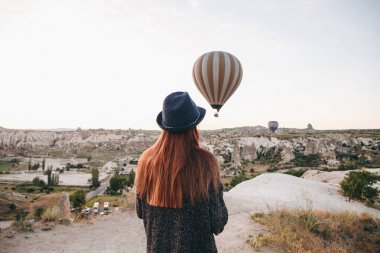 Şapkalı bir turist kız sıcak hava balonları Türkiye Kapadokya'da üzerinde gökyüzünde uçan hayran. Etkileyici görüş.