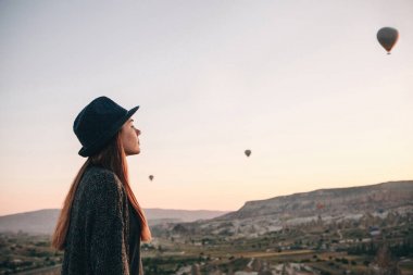 Şapkalı bir turist kız sıcak hava balonları Türkiye Kapadokya'da üzerinde gökyüzünde uçan hayran. Etkileyici görüş.