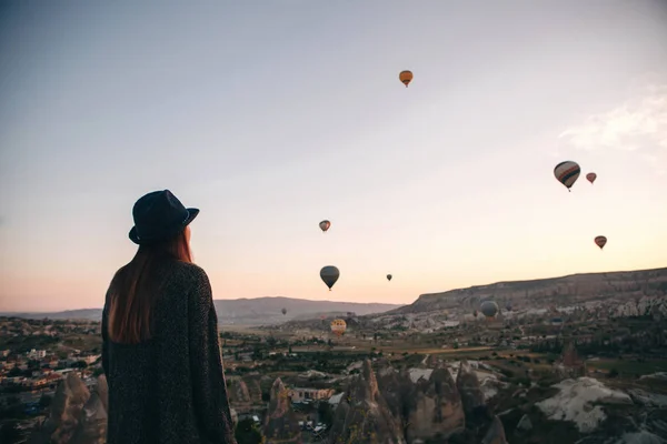 Uma turista de chapéu admira balões de ar quente voando no céu sobre a Capadócia, na Turquia. Visão impressionante. . — Fotografia de Stock