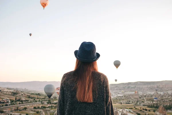 Uma turista de chapéu admira balões de ar quente voando no céu sobre a Capadócia, na Turquia. Visão impressionante. . — Fotografia de Stock