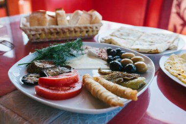 Yakın çekim. Domates, peynir, rulo, siyah ve yeşil zeytin ve patlıcan oluşan bir tabakta Servis Kahvaltı.