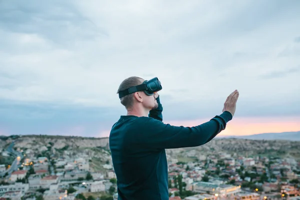 A man in virtual reality glasses on the background of a sunset over the city. Concept of future technologies. Modern technologies.