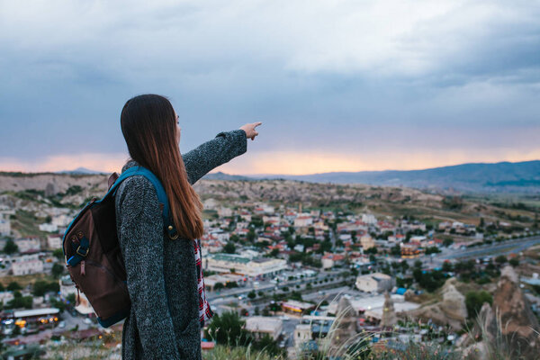 Young woman tourist with high point showing hand at sunset over the city of Goreme in Turkey. Cappadocia. Tourism, rest, vacation.