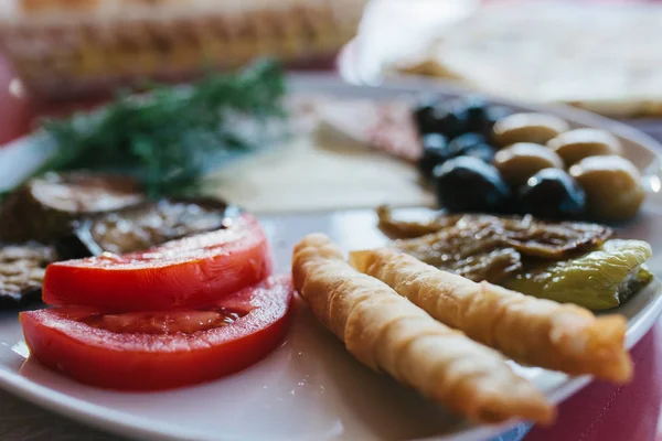 Close-up. Breakfast on a plate consisting of tomato, cheese, roll, black and green olives and eggplant. — Stock Photo, Image