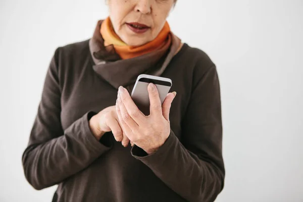 Una anciana moderna positiva sostiene un teléfono celular y lo está usando. La generación más antigua y la tecnología moderna . — Foto de Stock