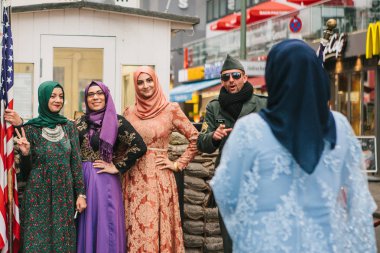 Berlin, 1 Ekim 2017: Pozitif huzurlu neşeli güzel Arap kadınlar geleneksel kostümleri iletişim ve checkpoint Charlie yanında Amerikan askerleri ile fotoğraf çekmek