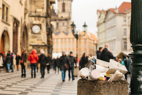 A crowded trash can on Pragues main square during the Christmas break. Many people are blurry in the background. Pollution of city streets with trash on holidays.