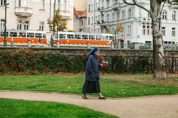 Praga, 25 settembre 2017: Una suora con la Sacra Bibbia in mano cammina lungo la strada sullo sfondo dell'architettura della città e del tram. Autentico. Stile di vita . — Foto Stock