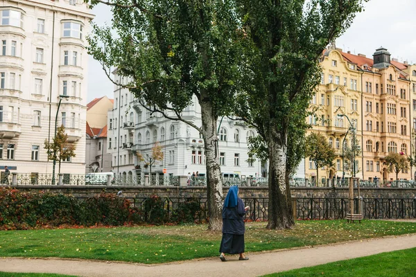 Praga, 25 de septiembre de 2017: Una monja con la Santa Biblia en la mano camina por el camino a lo largo de la calle contra el telón de fondo de la arquitectura de la ciudad. Auténtico. Estilo de vida . — Foto de Stock
