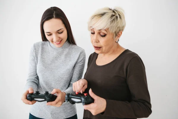 The elderly woman asks the young girl how to use the joystick for video games and shows her finger on the buttons. Modern technologies and people. Teaching older generation the use of technology.