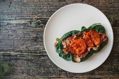 Üstten Görünüm. Jambon, kızarmış domates ve yeşillik bir ahşap yüzeyde bir tabakta lezzetli ve besleyici sandviç.