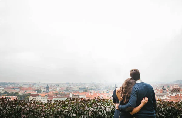 Uitzicht vanaf de achterkant. Een liefdevolle jonge mooie paar omhelzing tegen de achtergrond van een prachtig uitzicht van Praag. Sluiten van gevoelens en emoties tussen mensen. — Stockfoto
