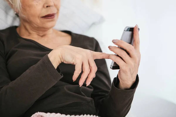 Una anciana moderna positiva sostiene un teléfono celular y lo está usando. La generación más antigua y la tecnología moderna . — Foto de Stock