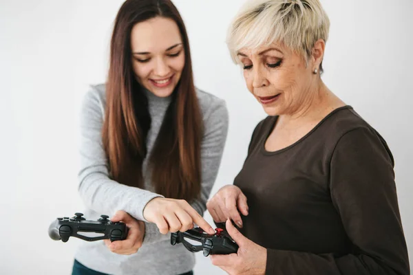 Uma jovem explica a uma mulher idosa como usar o joystick para jogos de vídeo. Passatempo conjunto. Tecnologias e pessoas modernas. Comunicação da avó com sua neta — Fotografia de Stock