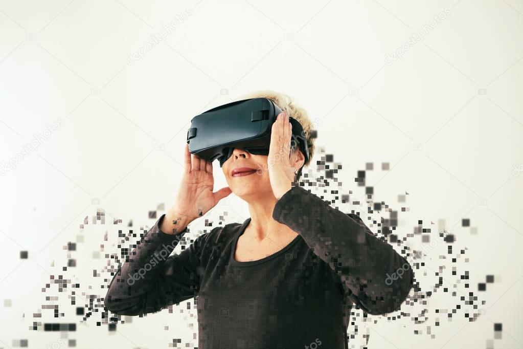 An elderly woman in virtual reality glasses is scattered by pixels. Conceptual photography with visual effects with an elderly person using modern technology.